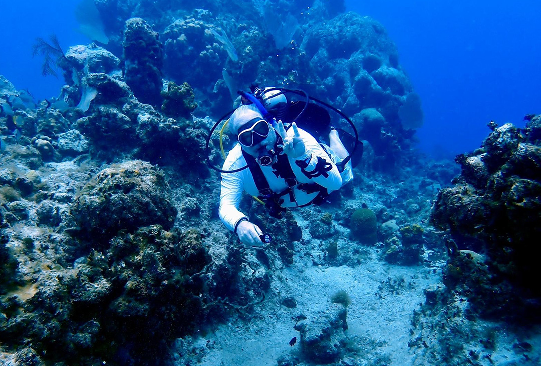 Underwater scuba diver makes the Hook 'em Horns hand sign.