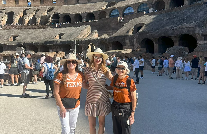 A group of three visitors on the floor of the Roman Coliseum.