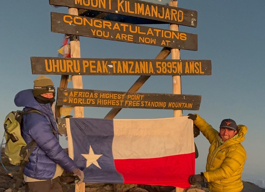 Two people hold a Texas flag at the summit of Mount Kilimanjaro