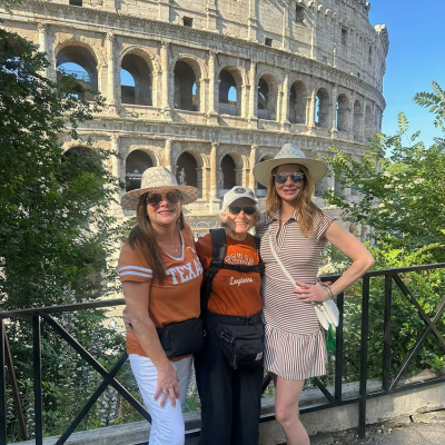 A mother and two daughters pose in burnt orange in front of the Roman Coliseum. 