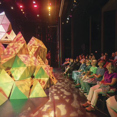 A massive geometric set piece protrudes into the watching audience, lit in shades of pink and green.