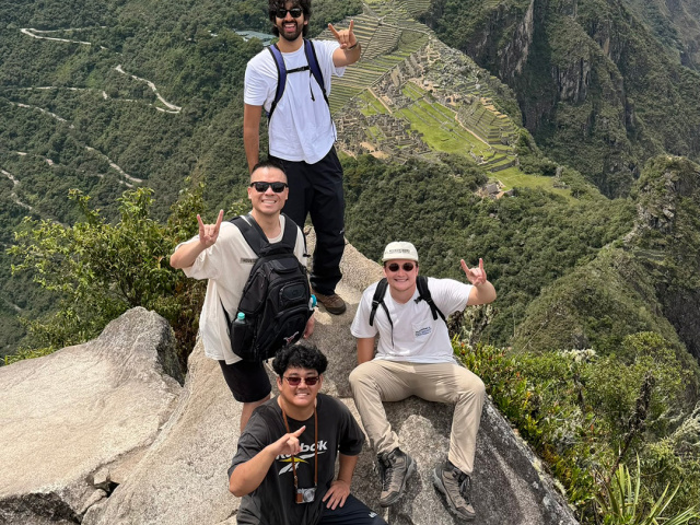 Four men high above Machu Pichu making the Hook 'em Horns hand sign.