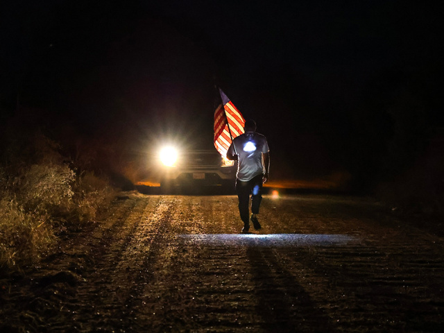 An overnight runner holding a USA flag in the Rivalry Relay.