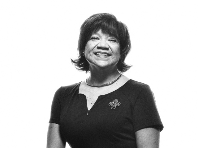 Woman on a black background wearing a black dress with a Longhorn broach.