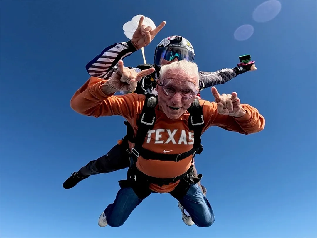Two men sky diving, each flashing the Hook 'em Horns hand sign.