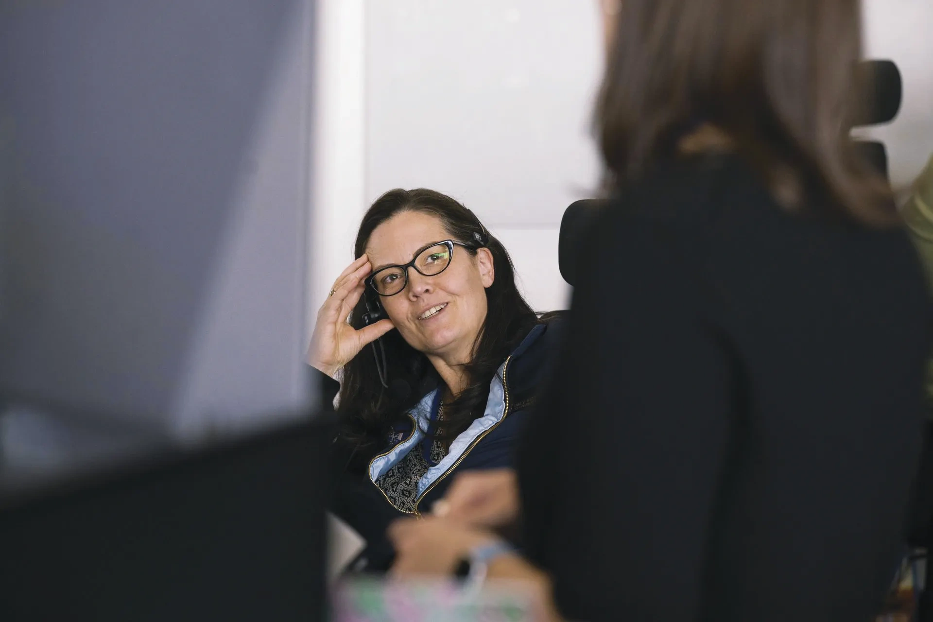 A woman in glasses leans her head to the right into her hand.