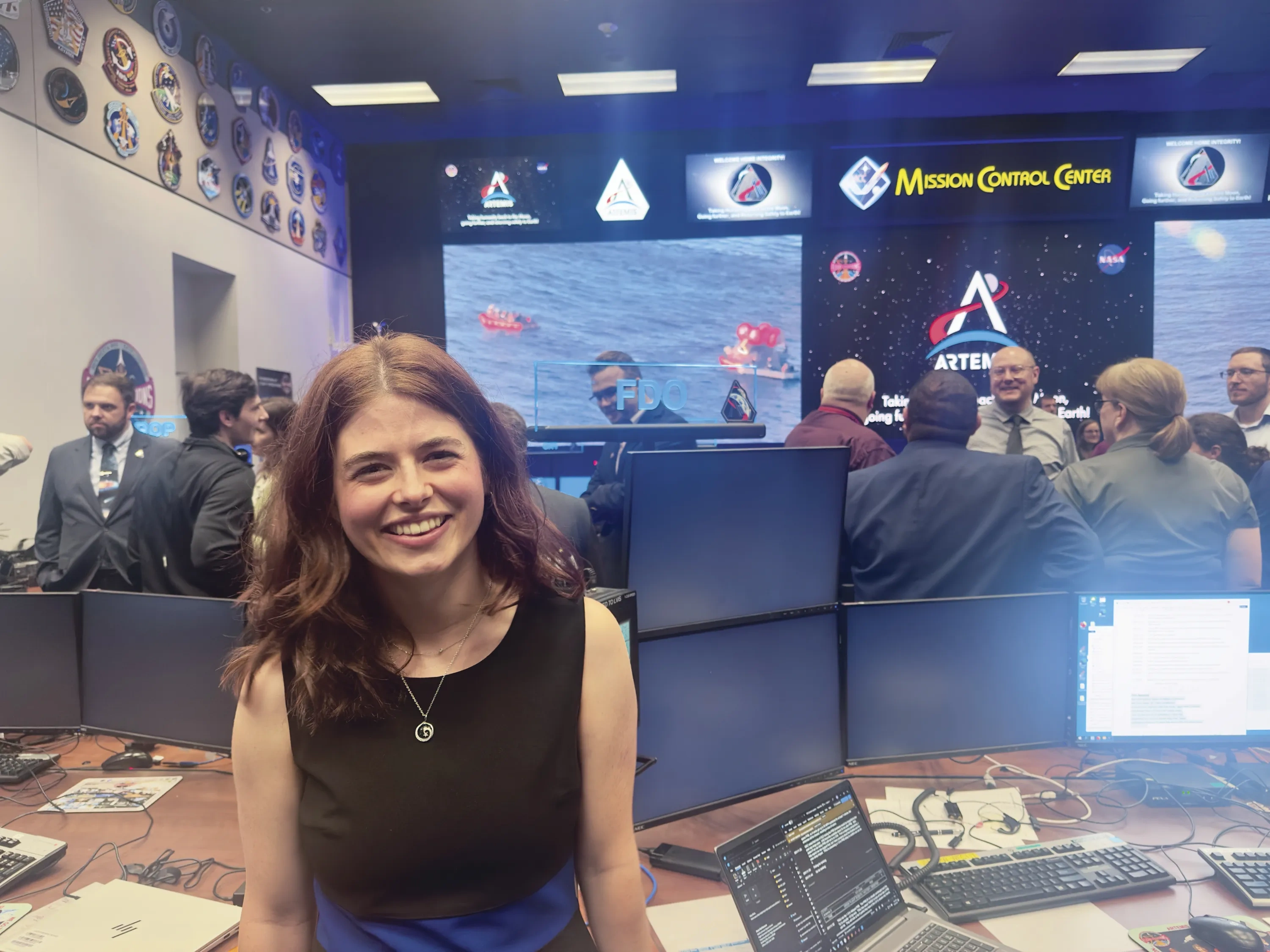 A woman poses in Mission Control with a video feed of the lander splashdown behind her.