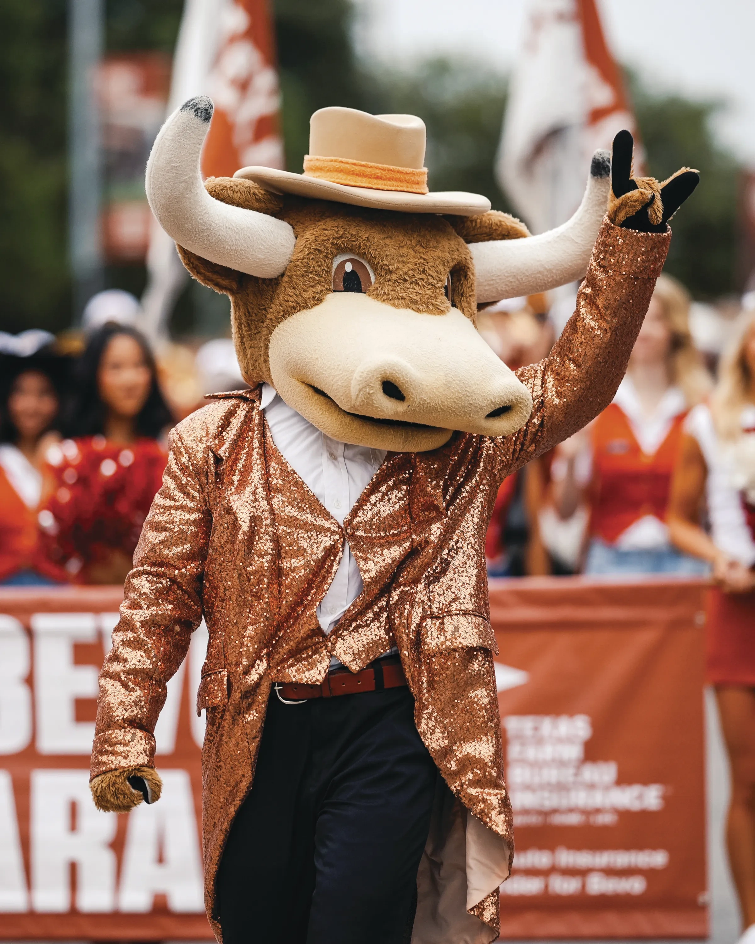 A stuffed Longhorn mascot in a sparkly burnt-orange suit waves to a crowd of fans.