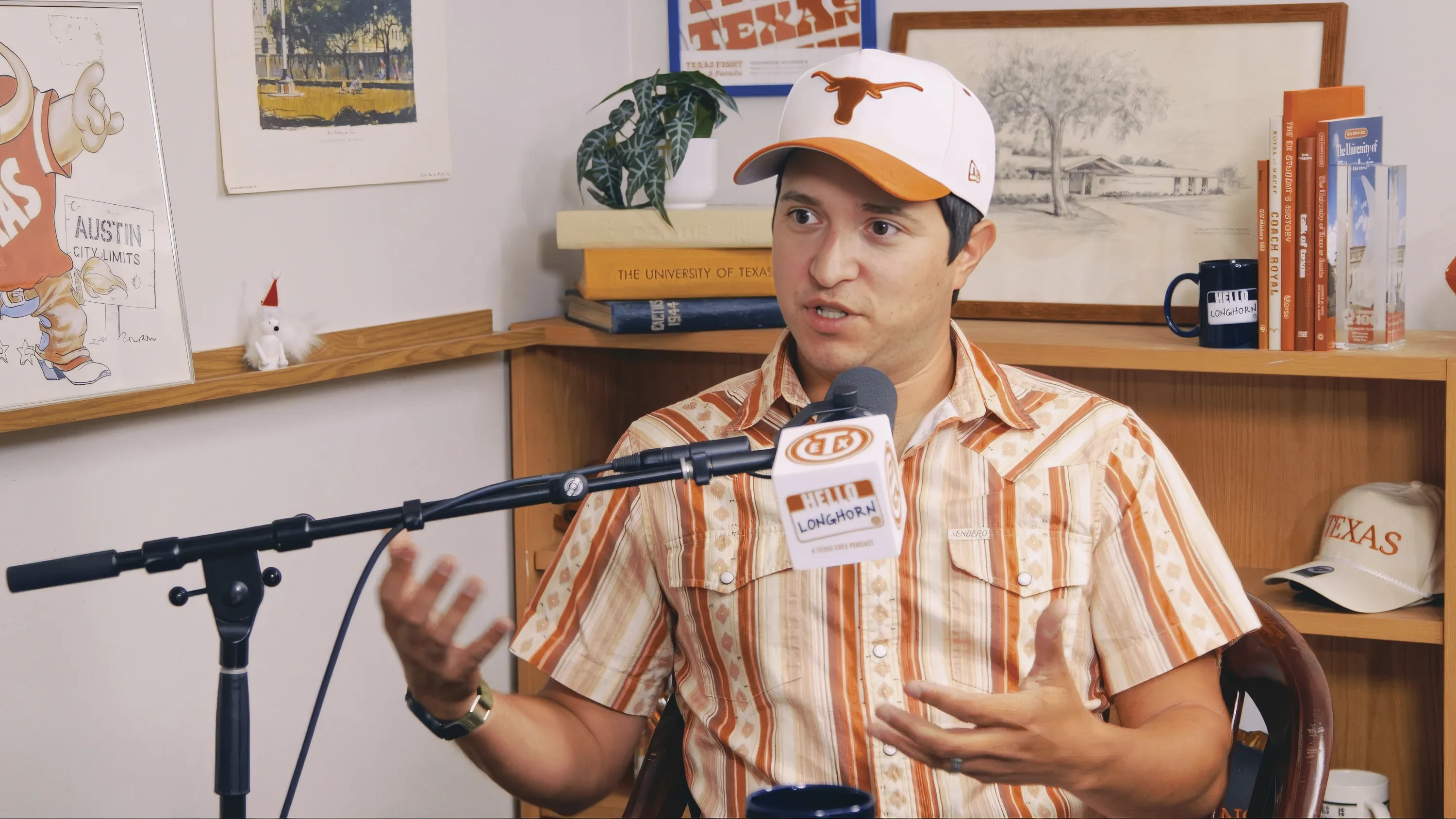 A man sits in front of a microphone recording a podcast and gesturing with his hands.