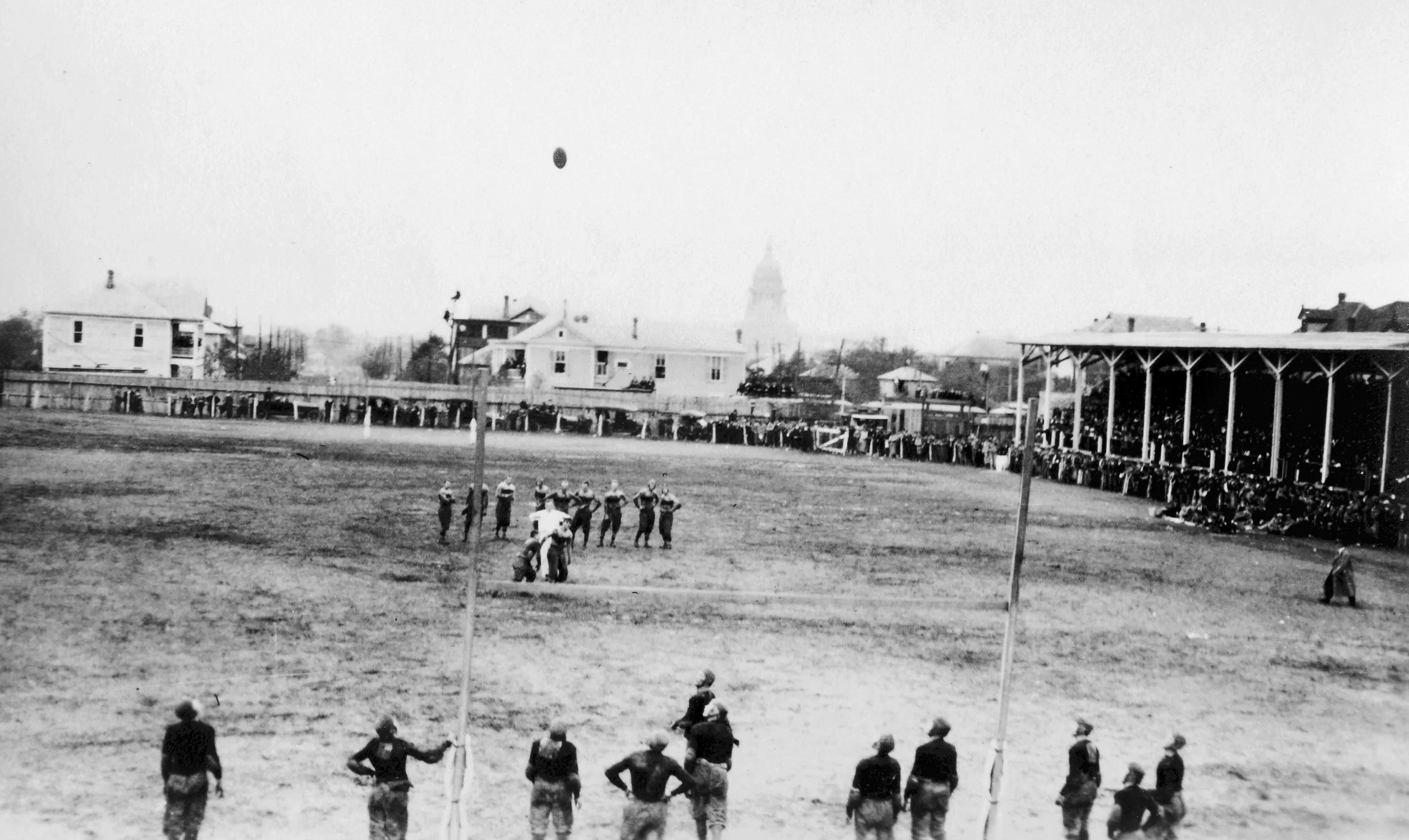 An archival photo over a grass football field of the Texas Capitol silhouetted in the distance, 1914.