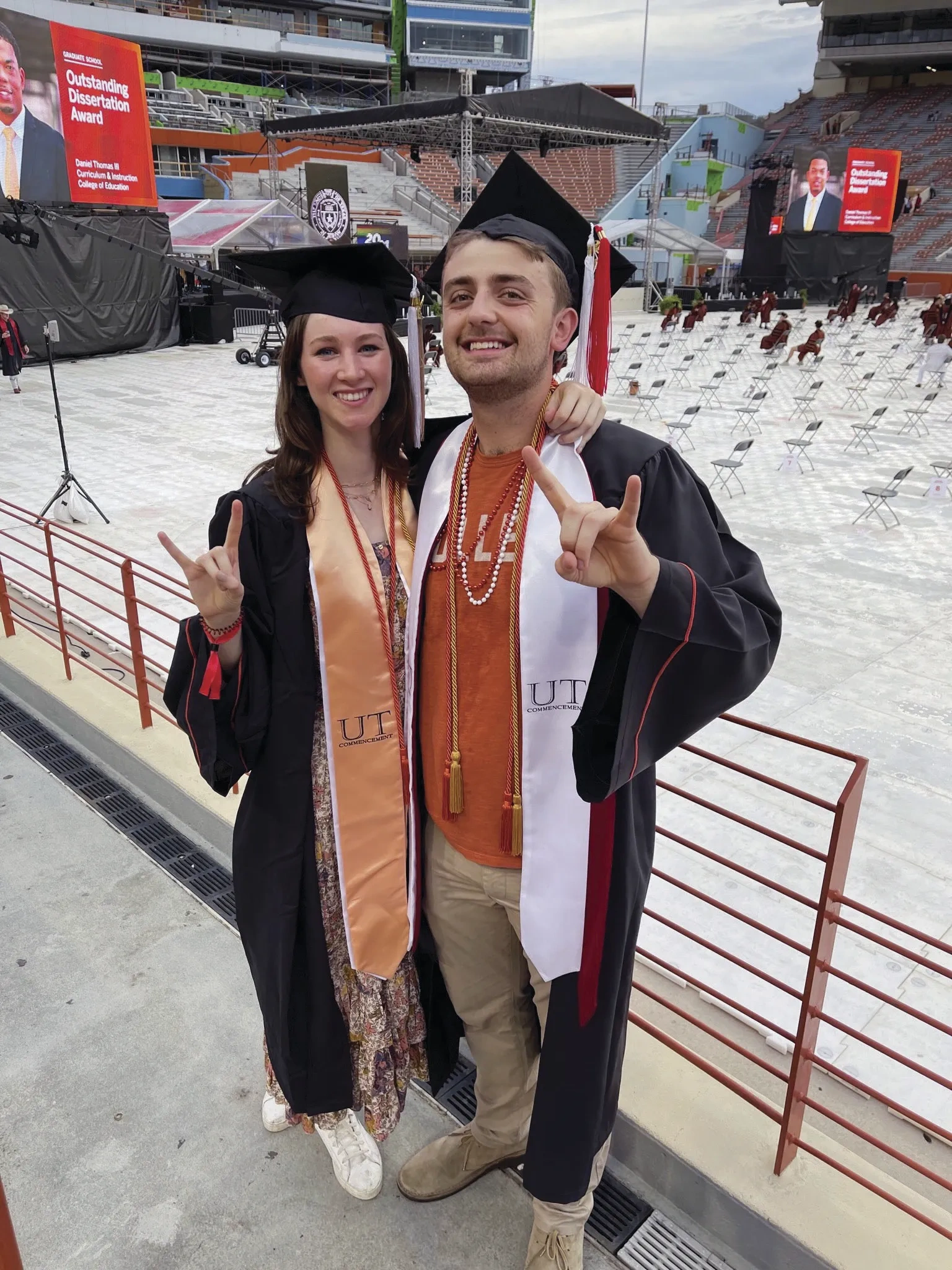 A man and a woman pose at a college graduation in caps, gowns, and stoles.