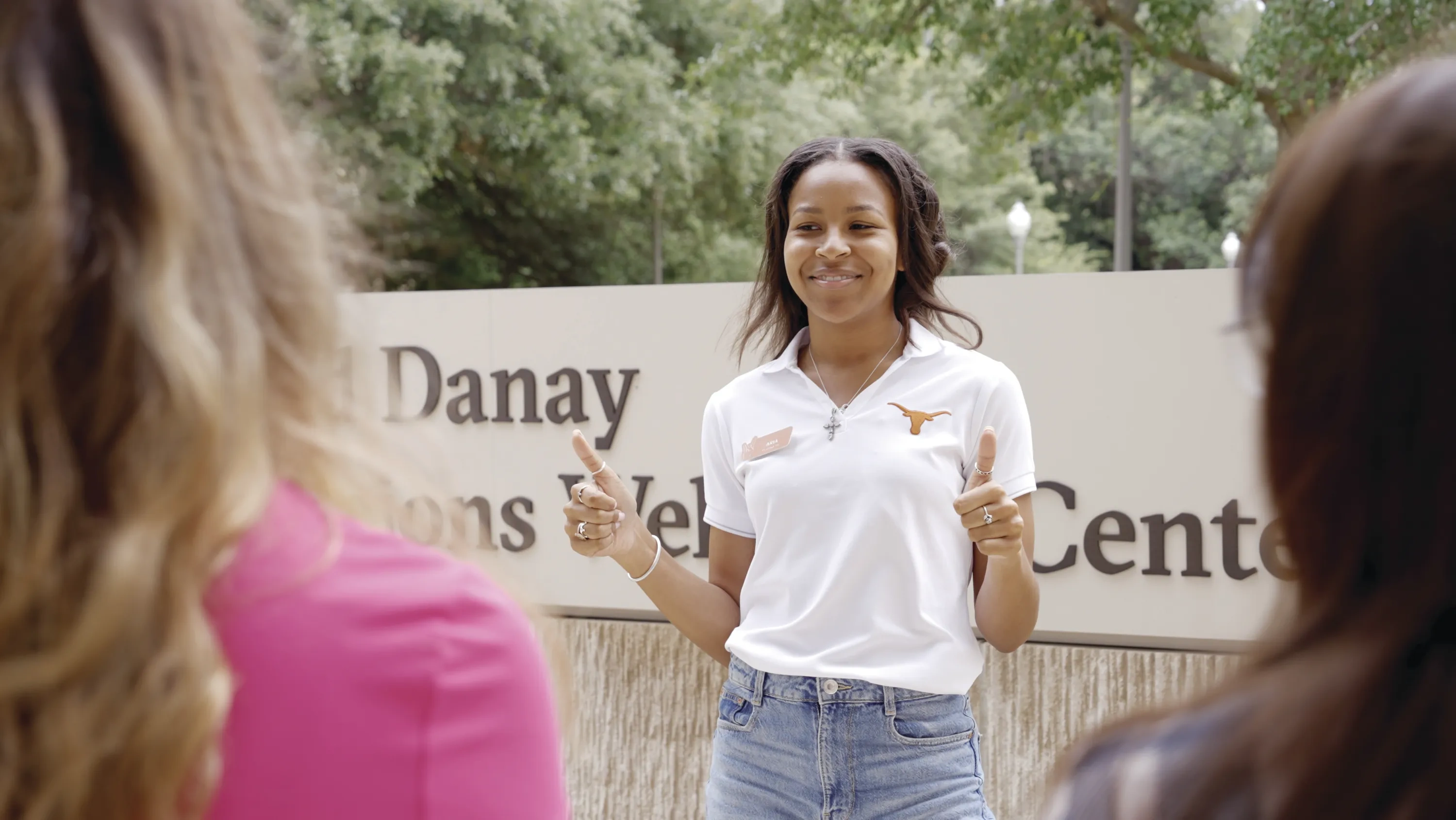 A female student wearing a white polo with a Longhorn logo leads a tour of the UT campus.