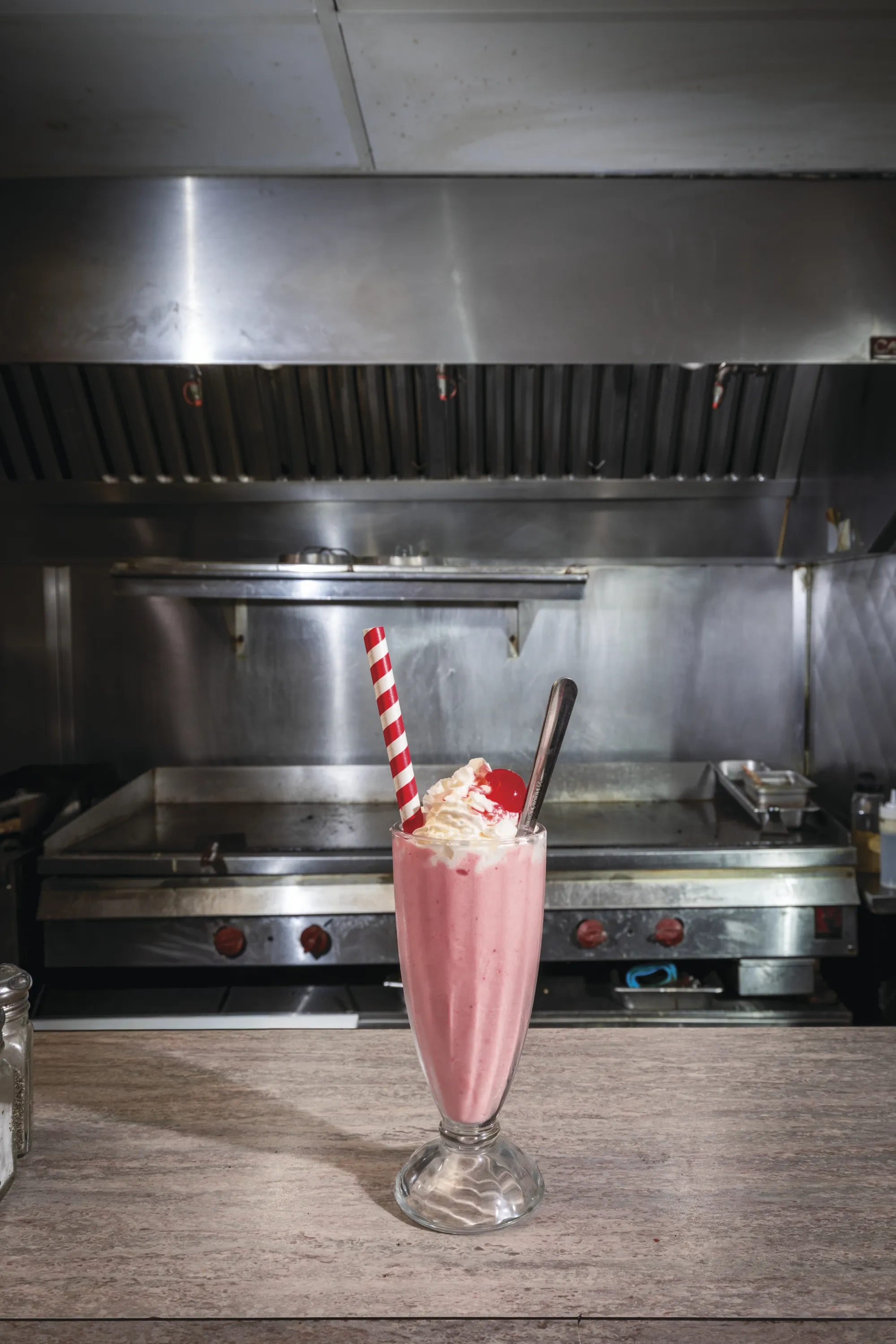 A strawberry milkshake with whipped cream, a cherry, and a red and white striped paper straw.